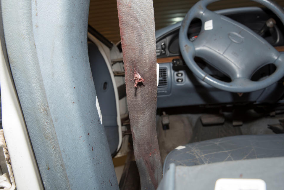 A bullet hole is seen on a bloodied seat belt.