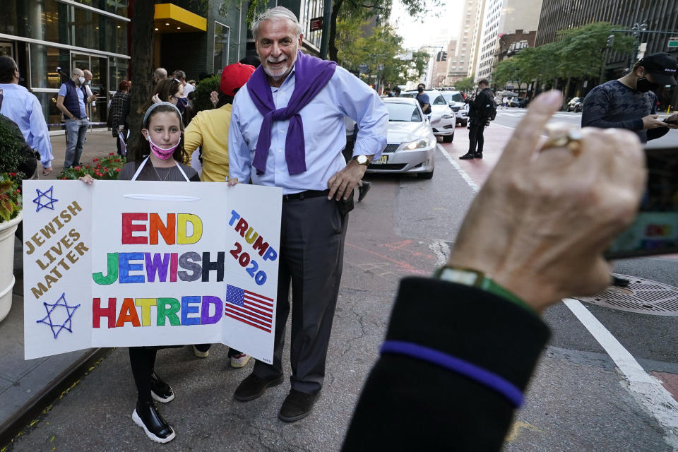A young girl poses for a cell phone photo with a homemade sign as she joined protesters outside the offices of New York Gov. Andrew Cuomo, Thursday, Oct. 15, 2020, in New York. Three Rockland County Jewish congregations are suing New York state and Gov. Andrew Cuomo, saying he engaged in a "streak of anti-Semitic discrimination" with a recent crackdown on religious gatherings to reduce the state's coronavirus infection rate. (AP Photo/Kathy Willens)