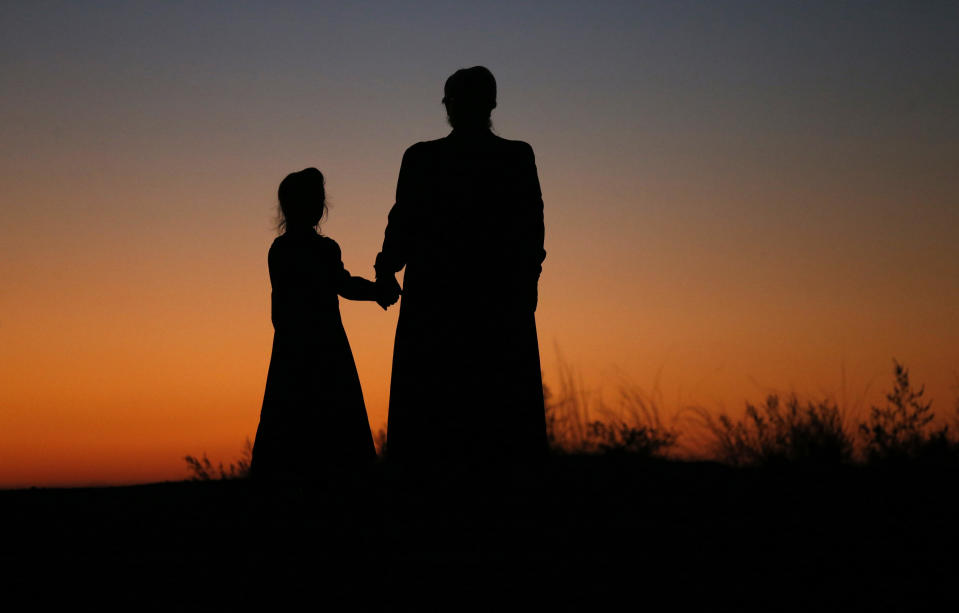 FILE - In this Oct. 25, 2017, file photo, a woman and a young girl hold hands for a photograph, in Colorado City, Ariz. They are members of a community on the Utah-Arizona border that has been home for more than a century to a polygamous sect that is an offshoot of mainstream Mormonism. The recent slaying in Mexico of nine people who belonged to a Mormon offshoot community where some people practice polygamy shines a new spotlight on the ongoing struggle for the mainstream church to fight the association with plural marriage groups because of its past. (AP Photo/Rick Bowmer, File)