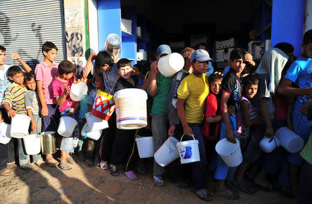 FILE PHOTO: Boys carry buckets as they queue to receive free food for their first iftar, or breaking fast, during the Muslim fasting month of Ramadan in Raqqa province, eastern Syria July 10, 2013. REUTERS/Nour Fourat/File Photo