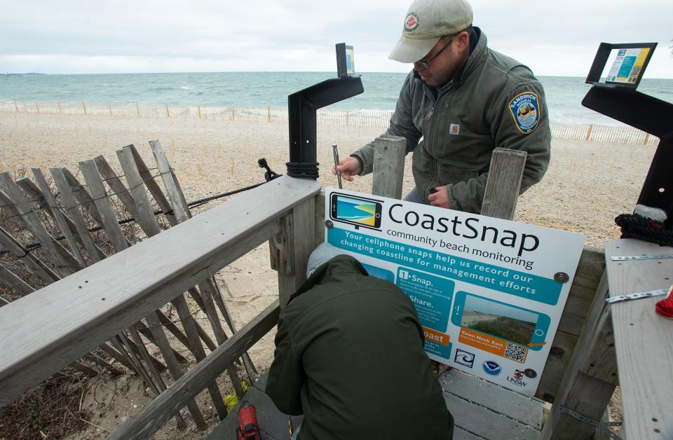 Josh Wrigley ,top, and Walter Fagnant with the town of Sandwich bolt a new CoastSnap sign to the end of one of the beach walkways at Town Neck Beach on Wednesday. Beachgoers are encouraged to use the phone supports to snap a photo in each direction of the beach and then upload them via a QR code on the sign. The photos are intended to help scientists monitor shoreline change.