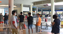 A safe-distancing enforcement officer wearing a red armband watches over customers lining up to buy take-away food at a food court in Singapore on Saturday, April 18, 2020. The officers have been deployed throughout the Southeast Asian city-state to ensure people maintain distance from one another as it grapples with a spike in coronavirus cases. (AP Photo/YK Chan)