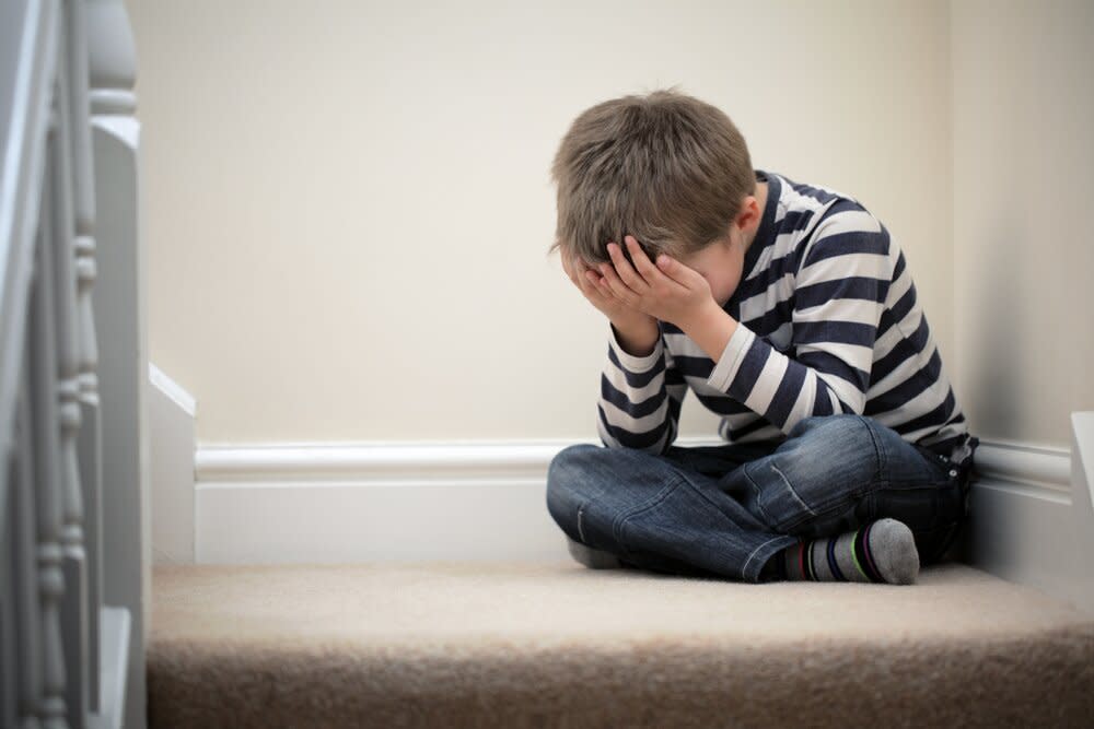 Upset boy sitting in corner covering face