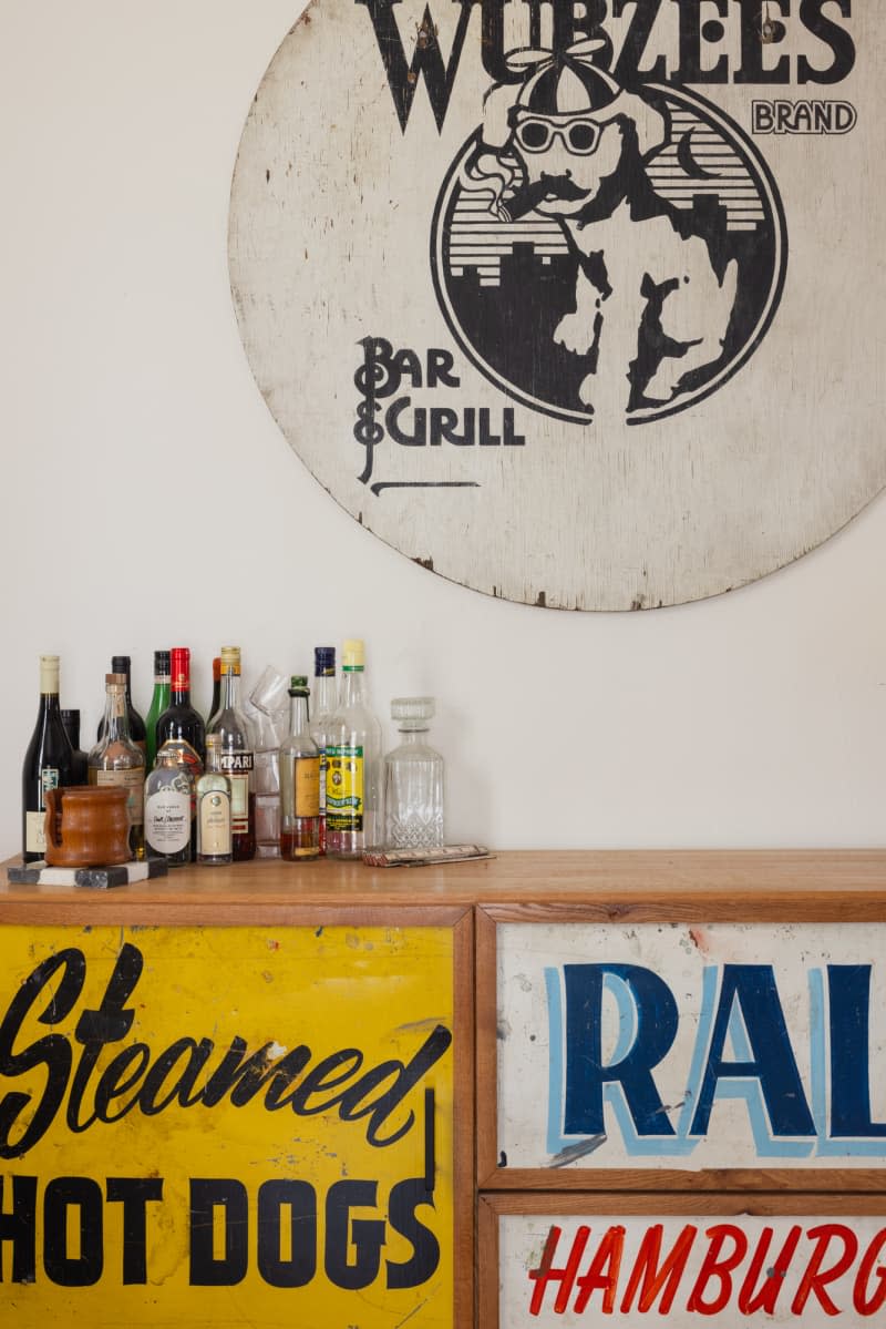 Bar art hung on white wall above sideboard decorated with signs holding liquor.