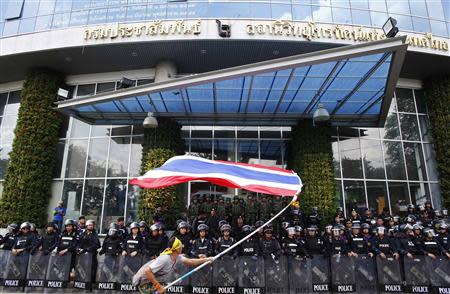 An anti-government protester waves a national flag in front of riot police officers and soldiers guarding the entrance of the National Broadcast Services of Thailand (NBT) television station in Bangkok May 9, 2014. REUTERS/Athit Perawongmetha