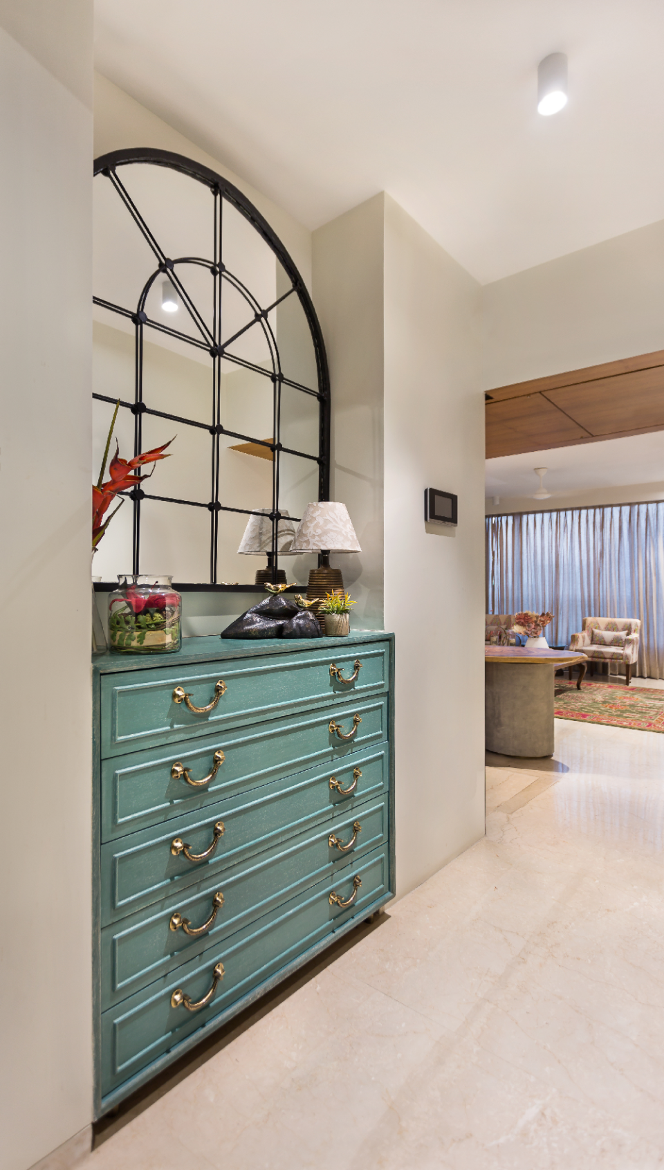 In the foyer, a niche presents an opportunity for neatly tucked away storage: a handmade, teak chest of drawers that’s spruced up with an arched, metal-framed mirror and decor pieces.