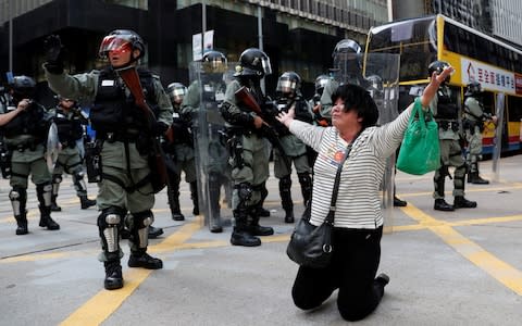 A woman cries and prays in front of riot police during an anti-government protest in Central Hong Kong - Credit: SHANNON STAPLETON/REUTERS