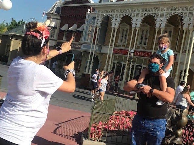 A family all wearing masks, stops for photos at Magic Kingdom.