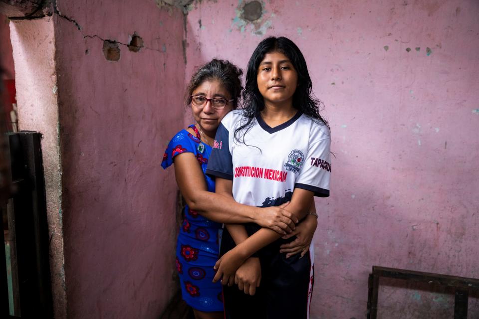 A woman stands with her arms around a young girl.