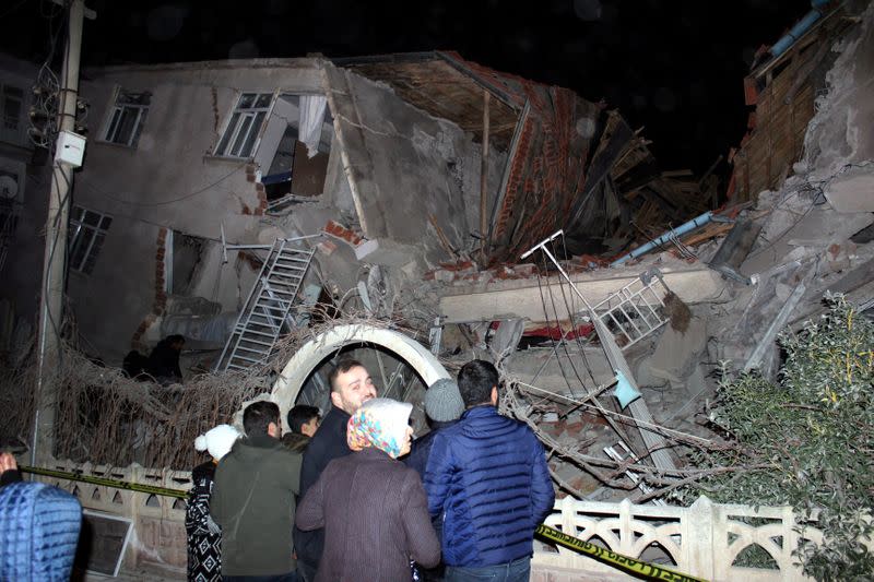 People stand outside a collapsed building after an earthquake in Elazig