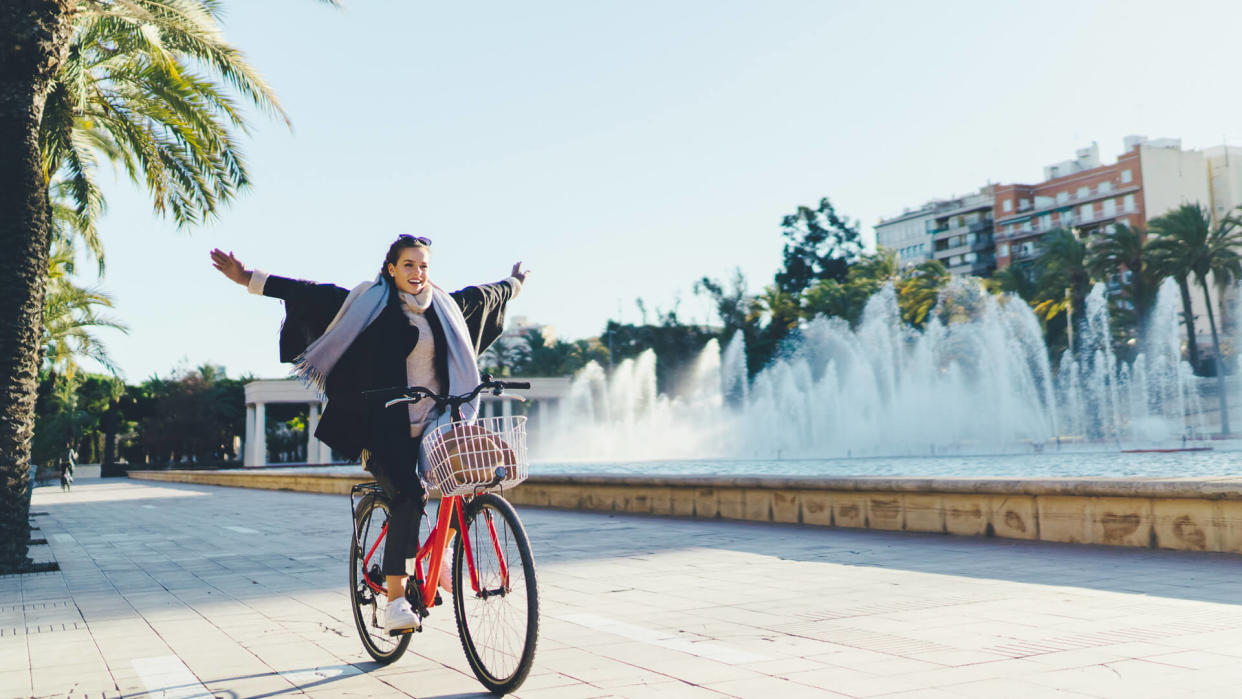 Happy woman with arms outstretched exploring Valencia on bicycle.