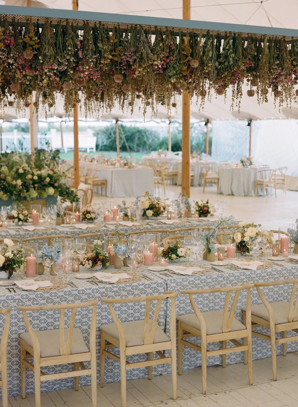 A wedding in a tent with blue tablecloths and florals hanging from the ceiling.