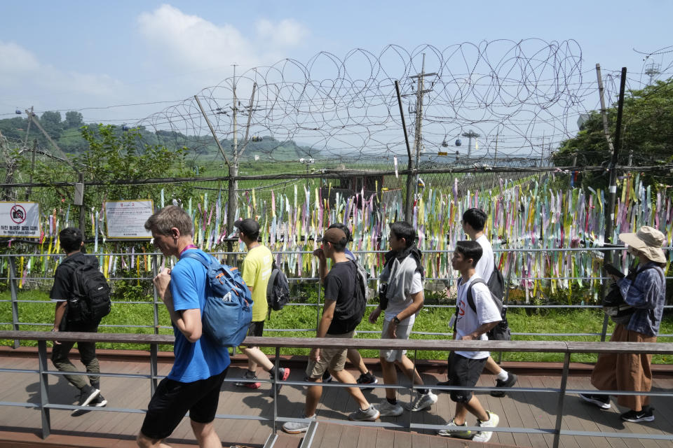 Visitors pass by a wire fence decorated with ribbons written with messages wishing for the reunification of the two Koreas at the Imjingak Pavilion in Paju, South Korea, near the border with North Korea, Wednesday, July 19, 2023. North Korea was silent about the highly unusual entry of an American soldier across the Koreas' heavily fortified border although it test-fired short-range missiles Wednesday in its latest weapons display. (AP Photo/Ahn Young-joon)
