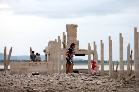 People walk through the ruins of a Buddhist temple which has resurfaced in a dried-up dam due to drought, in Lopburi, Thailand