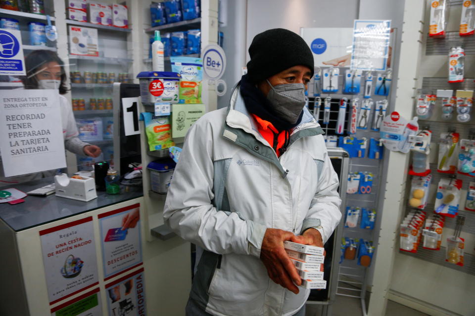 A person in a mask carries free COVID-19 test kits at a Madrid pharmacy. 