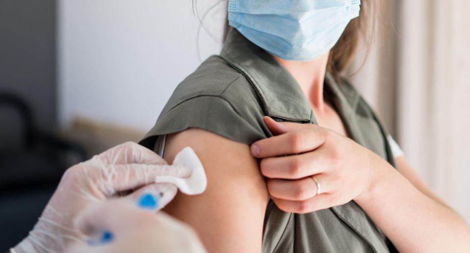 A woman wearing a face mask receives a vaccine.