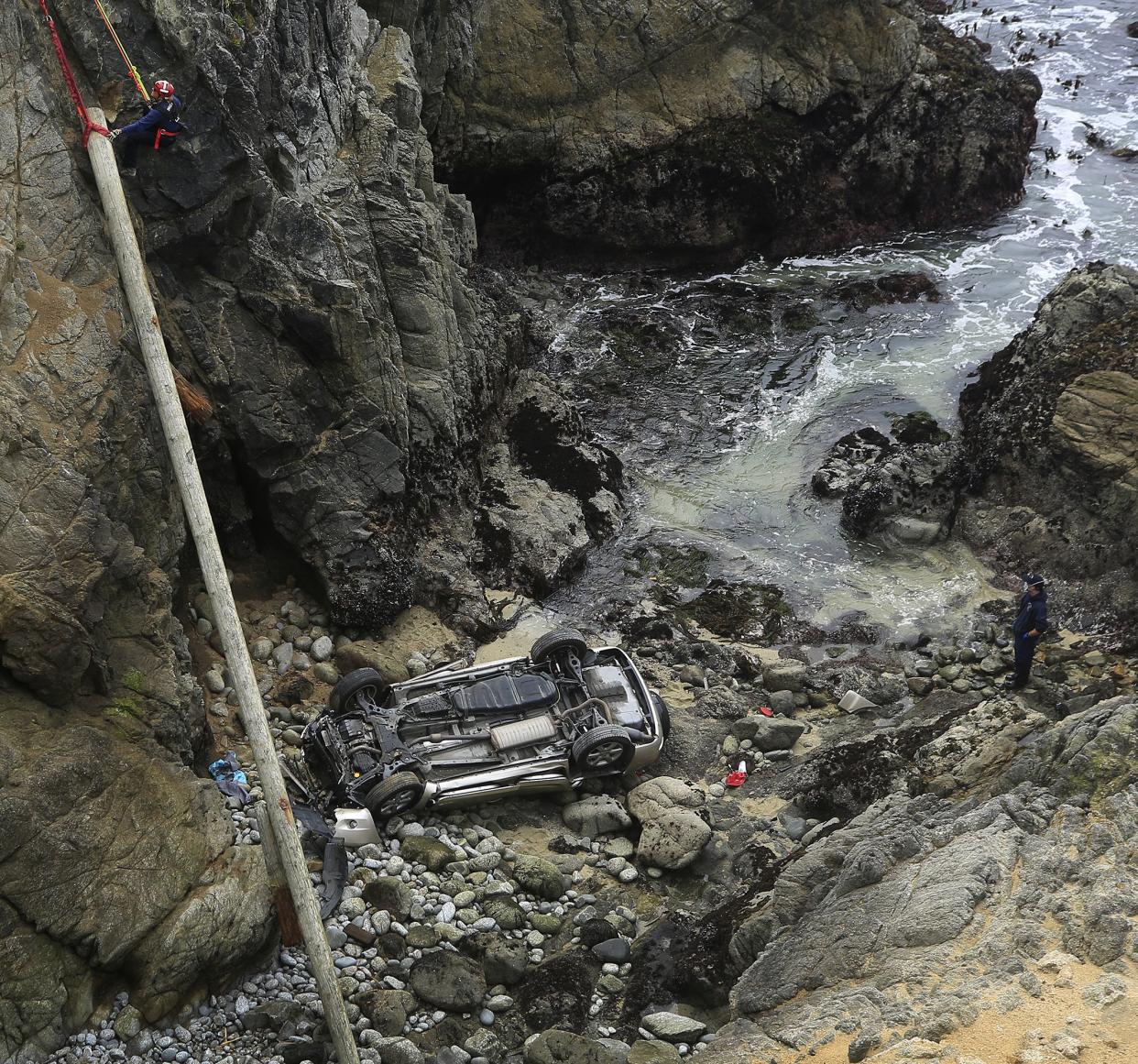 Bodega Bay firefighters work to secure the scene of a crash after a vehicle plummeted from the Bodega Head parking lot in Bodega Bay, Calif., through a wood barrier, left, landing upside down 100 feet to the rocky shoreline, killing two people in the SUV, Saturday, April 3. 