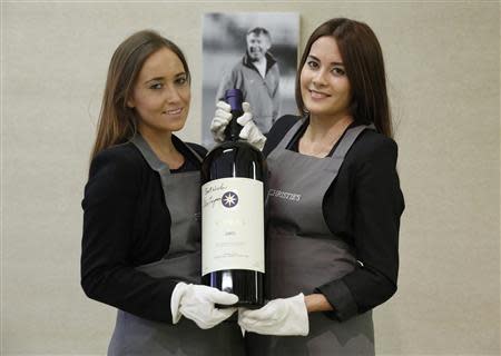 Employees pose with a six litre imperiale "Sassicaia 2005" wine, signed by retired Manchester United boss Alex Ferguson, at Christie's auction house in London April 14, 2014. REUTERS/Luke MacGregor