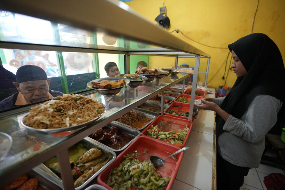 Una trabajadora sirve a los clientes en una tienda de comida en Bekasi, a las afueras de Yakarta, Indonesia, el jueves 2 de febrero de 2023. Casi un año después de que Rusia invadiera Ucrania, los altos precios de la comida castigan especialmente a los pobres del mundo. En Yakarta, los vendedores de comida saben que no pueden trasladar los incrementos de precio a clientes que ya tenían problemas económicos. (AP Foto/Achmad Ibrahim)