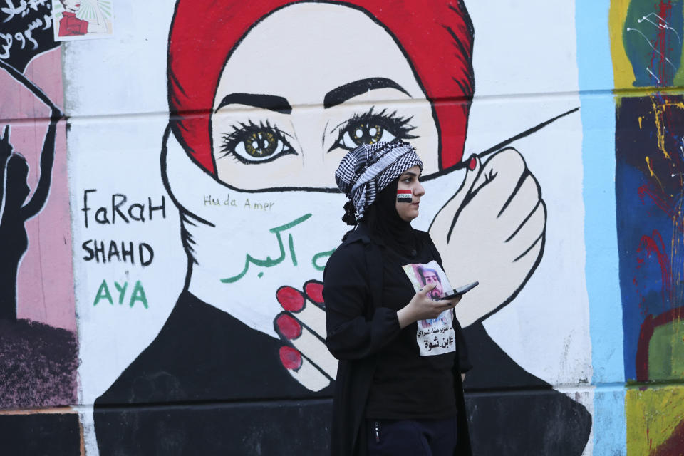 In this Sunday, Nov. 17, 2019 photo, a woman stands in front of graffiti at the Saadoun Tunnel, in Baghdad, Iraq. The tunnel that passes under Baghdad’s landmark Tahrir Square has become an ad hoc museum for Iraq's revolution: Young artists draw images and murals that illustrate the country’s tortured past, and the Iraq they aspire to. (AP Photo/Hadi Mizban)