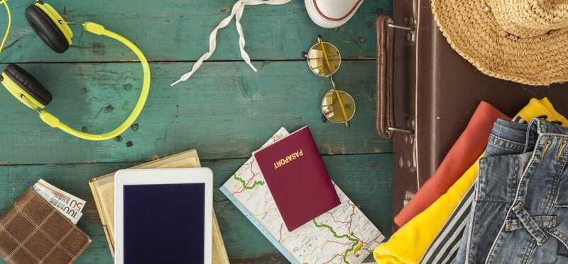 A top-down view of items being packed for a trip: passport, camera, map, sunglasses, suitcase