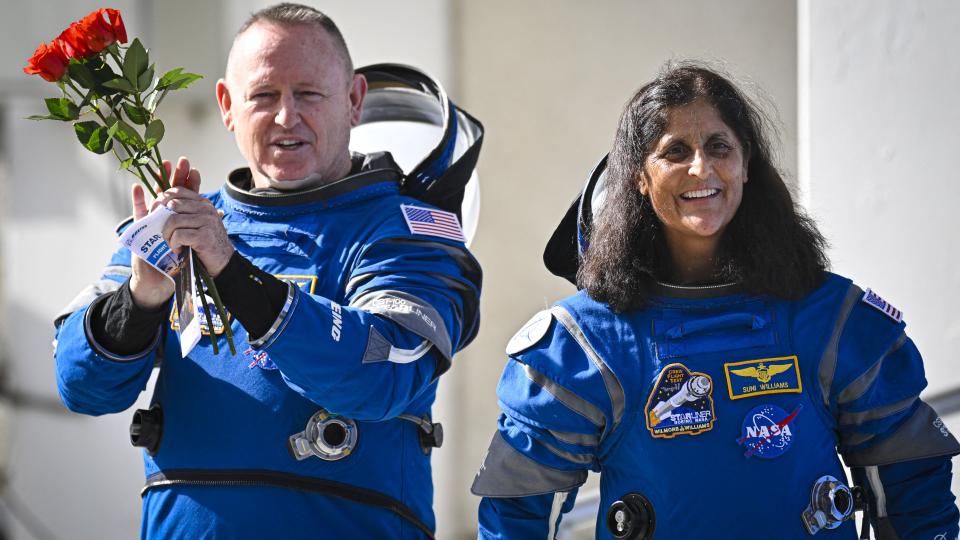 two astronauts in spacesuits.  the man on the left holds roses