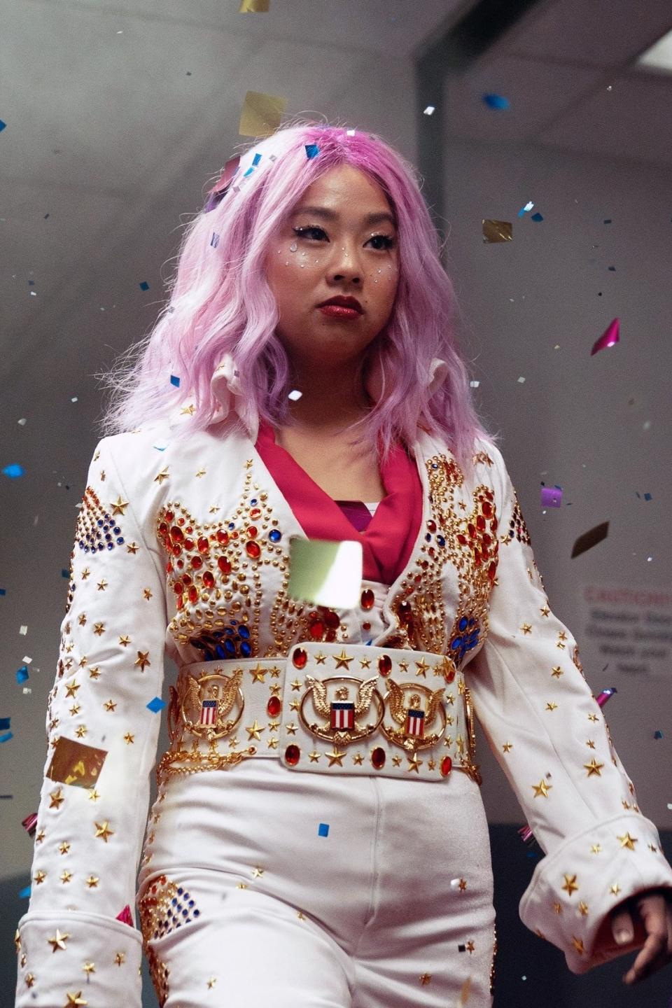 A person with vibrant hair in a decorated outfit walks confidently through a hallway amid falling confetti