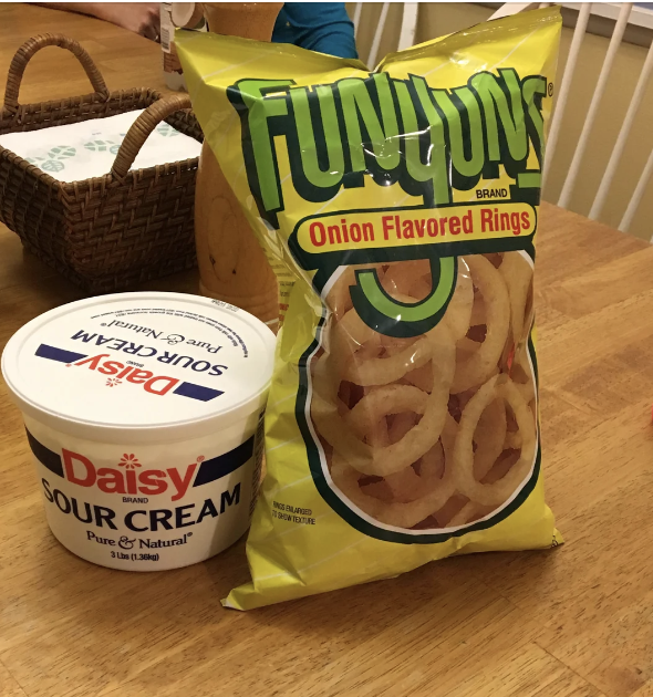 A tub of Daisy sour cream and a bag of Funyuns onion flavored rings sit on a wooden table, possibly ready for a snack or meal