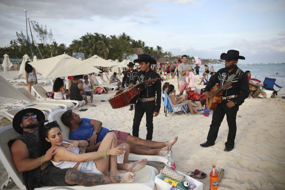 Roving musicians "Los Compas" approach a group of tourists on the shore of Mamitas beach, in Playa del Carmen, Quintana Roo state, Mexico, Tuesday, Jan. 5, 2021, amid the new coronavirus pandemic. Tens of thousands of American tourists descended on Mexico's glittering Caribbean beaches at the close of 2020 and the start of 2021, taking a break from the pandemic winter in the United States. (AP Photo/Emilio Espejel)