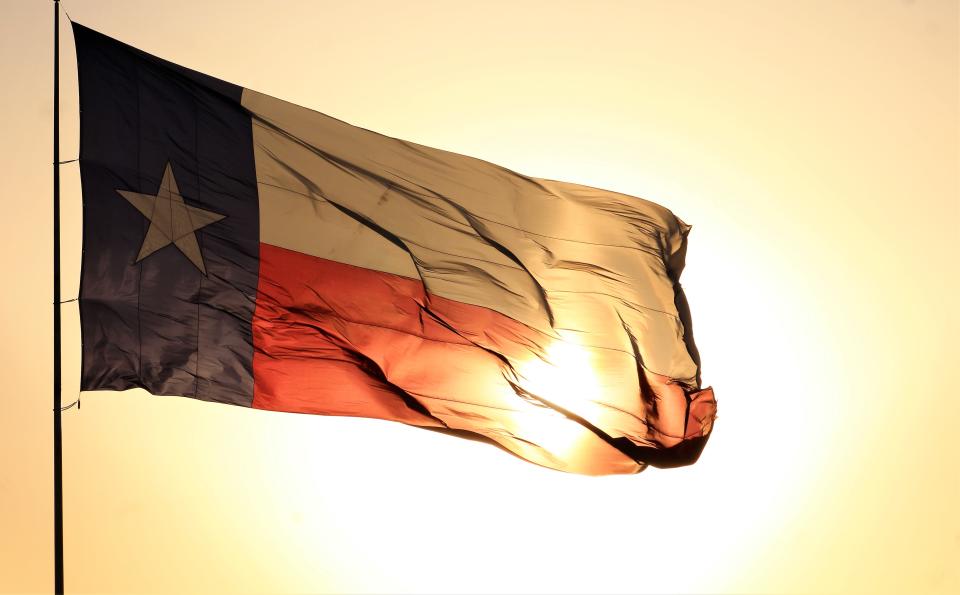 The sun shines through a large Texas flag.