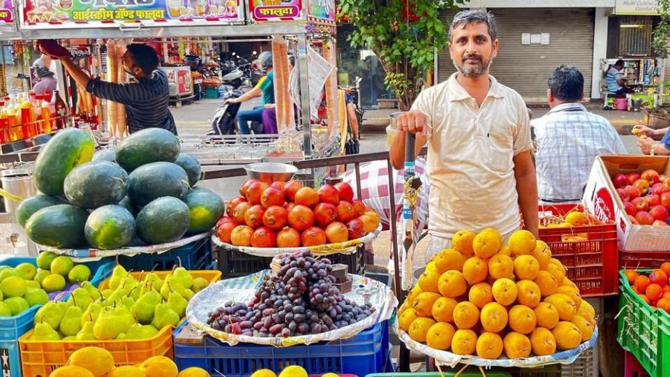 Arun Kumar stands at his fruit stand with neat piles of melon, pomegranate, grapes and more