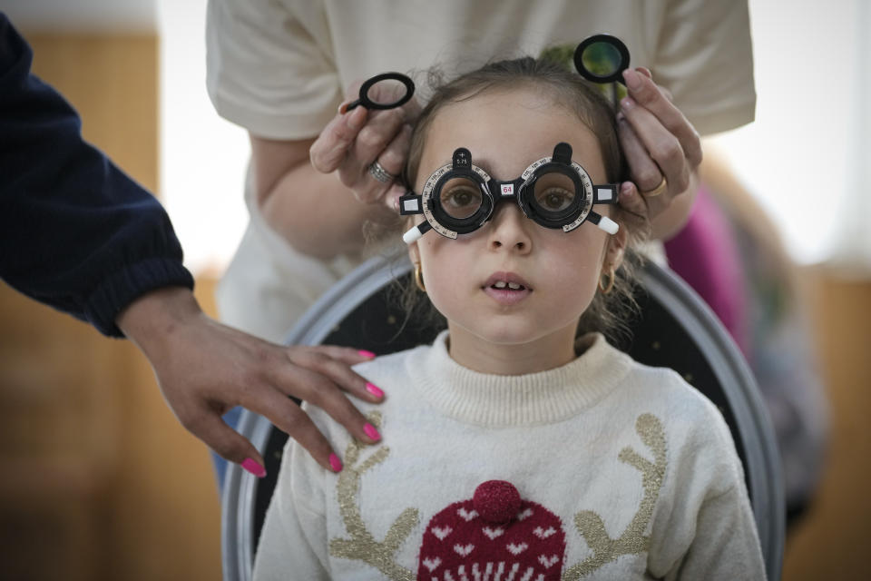 A woman holds her hand on her daughter during an eyesight examination performed by volunteer ophthalmologists working with the humanitarian organization Casa Buna, or Good House, in Nucsoara, Romania, Saturday, May 29, 2021. Dozens of disadvantaged young Romanian children got a chance to get their eyesight examined for the first time in their lives at an event in a remote village in the country's southern Carpathian Mountains.(AP Photo/Vadim Ghirda)
