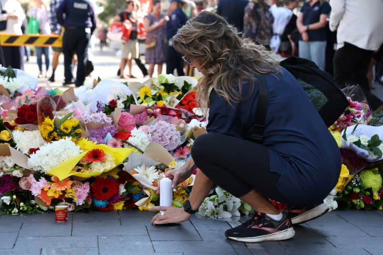 Une femme allume une bougie après avoir déposé des fleurs, le 14 avril 2024, en hommage aux victimes de l'attaque au couteau dans un centre commercial à Sydney (DAVID GRAY)