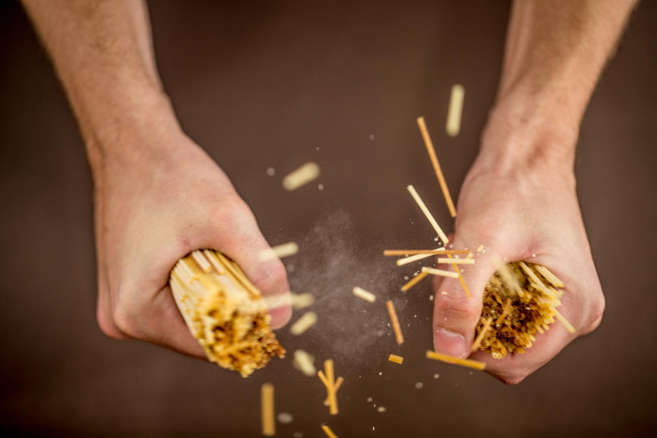 person breaking spaghetti in half with their hands