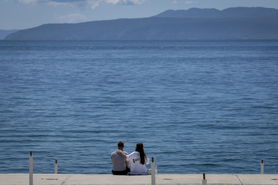 A couple sits at the seafront in Opatija, Croatia, Saturday, May 15, 2021. Croatia has opened its stunning Adriatic coastline for foreign tourists after a year of depressing coronavirus lockdowns and restrictions. (AP Photo/Darko Bandic)