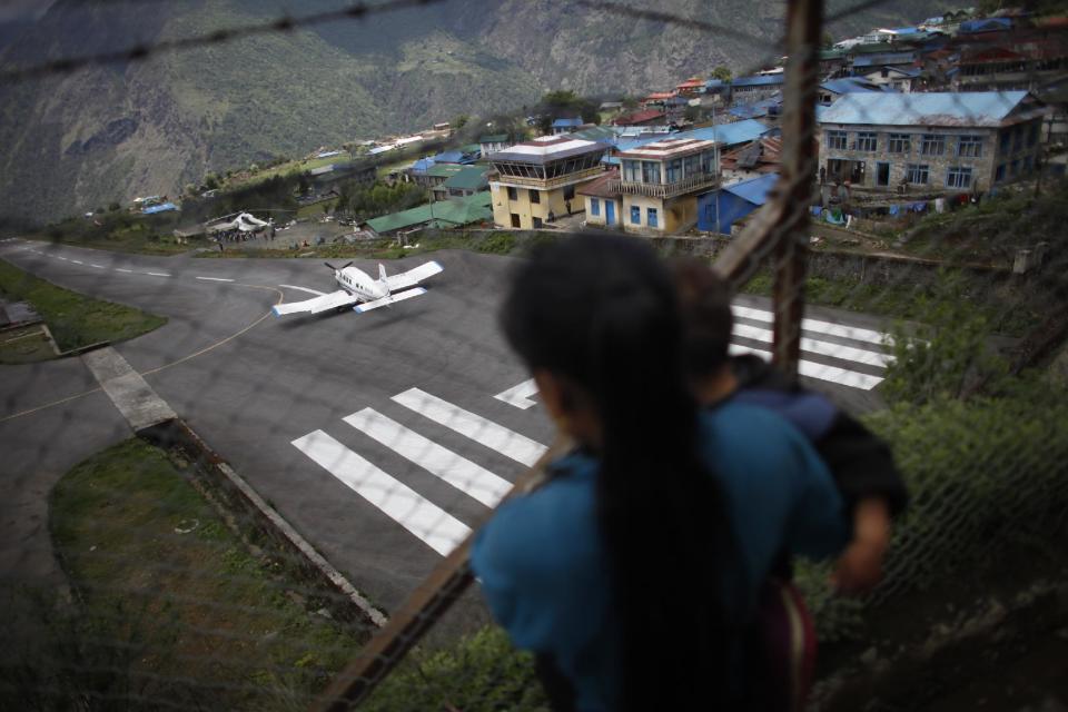 In this Friday, May 24, 2013 photo, a woman carrying her child watches a plane taking off en route to Katmandu from Lukla airport, Nepal. Carved out of side of a mountain, the airport was built by Sir Edmund Hillary in 1965, and at an altitude of 2,843 meters (9,325 feet) it has earned the reputation of being one of the most extreme and dangerous airports in the world. (AP Photo/Niranjan Shrestha)