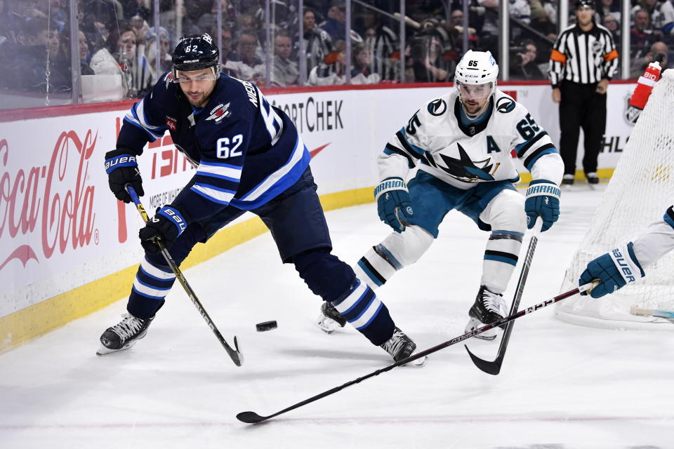 Winnipeg Jets' Nino Niederreiter (62) passes the puck past San Jose Sharks' Erik Karlsson (65) during second-period NHL hockey game action in Winnipeg, Manitoba, Monday April 10, 2023. (Fred Greenslade/The Canadian Press via AP)