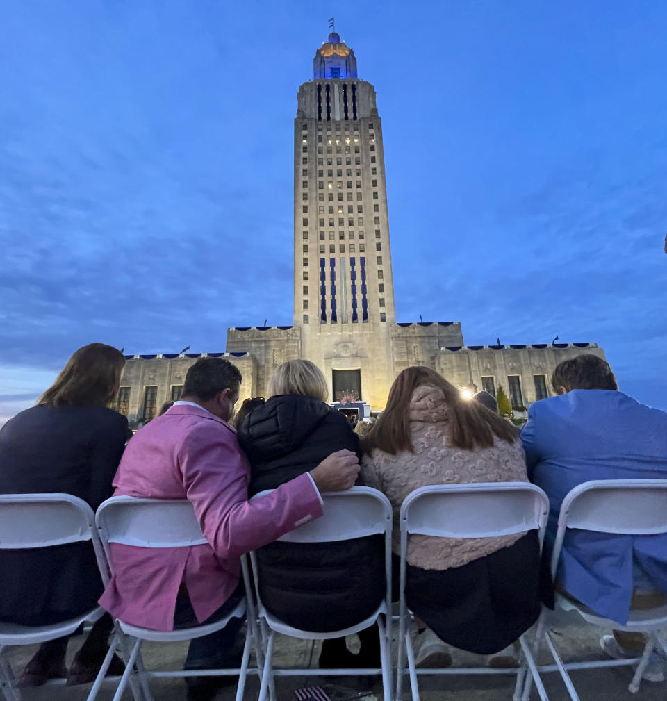 At twilight, people listen to Louisiana Republican Gov. Jeff Landry speak during his inauguration ceremony at the State Capitol building in Baton Rouge, La., Sunday, Jan. 7, 2024. The ceremony was moved because of forecasted rain on Monday, Jan. 8, the actual date Landry officially becomes governor. (AP Photo/Matthew Hinton)