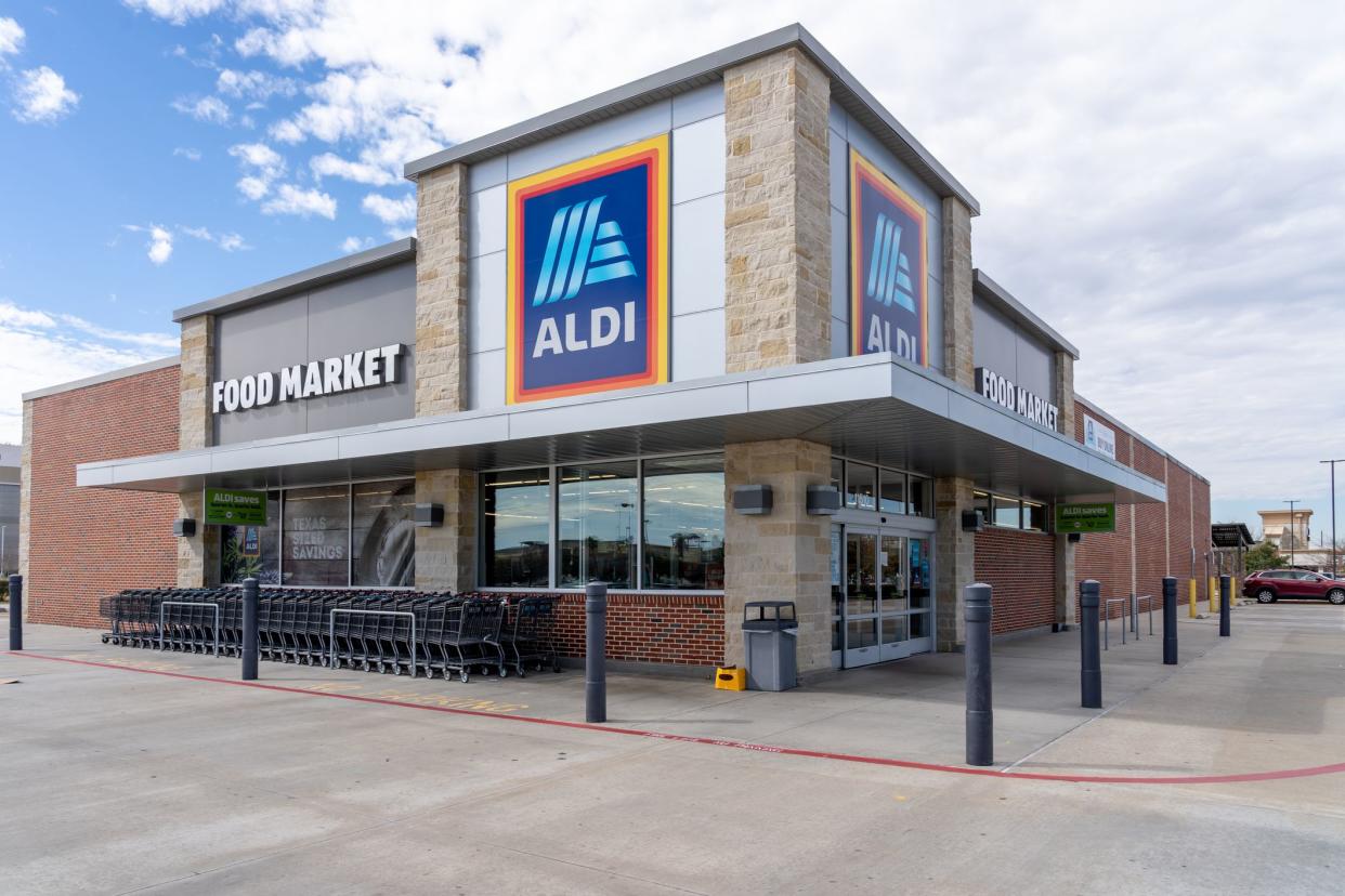Corner front exterior of an Aldi grocery store in pearland, texas, carts on the left and front doors on the right with lots of sidewalk around the building, parking spaces in the distant right and against a blue sky with white clouds