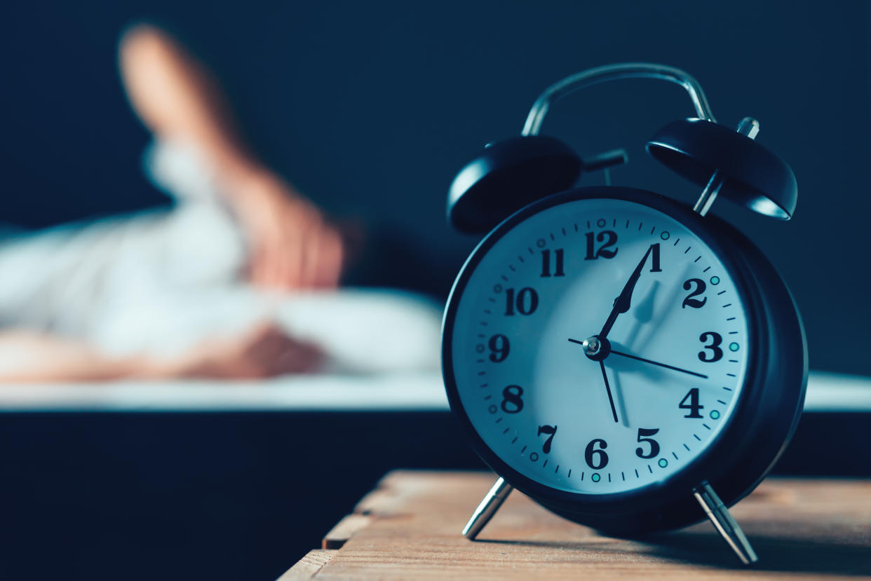 Sleeping disorder or insomnia concept, selective focus of vintage clock in bedroom and out of focus male person trying to fall asleep in bed