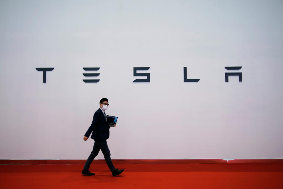 A man holding a computer walks past a sign of electric carmaker Tesla during a media day for the Auto Shanghai show in Shanghai, China April 20, 2021. REUTERS/Aly Song