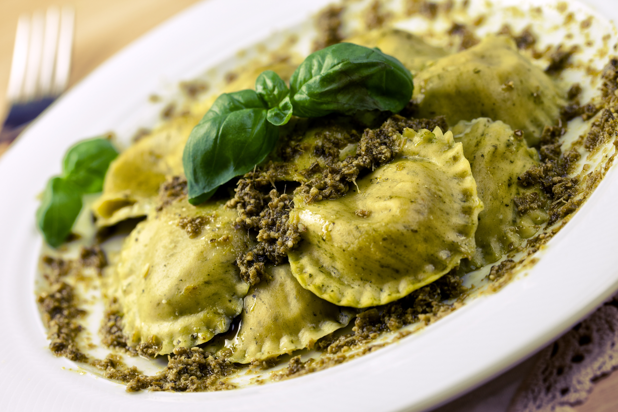 Closeup of spinach ravioli on a white porcelain plate, diagonal, selective focus, a fork on the table blurred in the background, top left