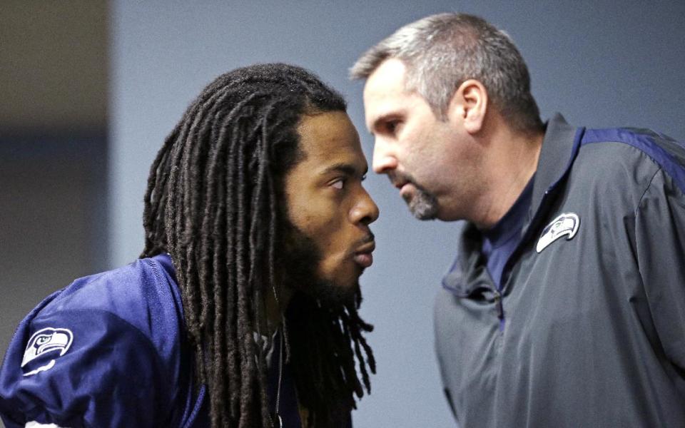 Seattle Seahawks' Richard Sherman, left, listens as Dave Pearson, team vice president of communications and broadcasting, whispers in his ear in the back of the room before an NFL football news conference Wednesday, Jan. 22, 2014, in Renton, Wash. The Seahawks play the Denver Broncos in the Super Bowl on Feb. 2. (AP Photo/Elaine Thompson)