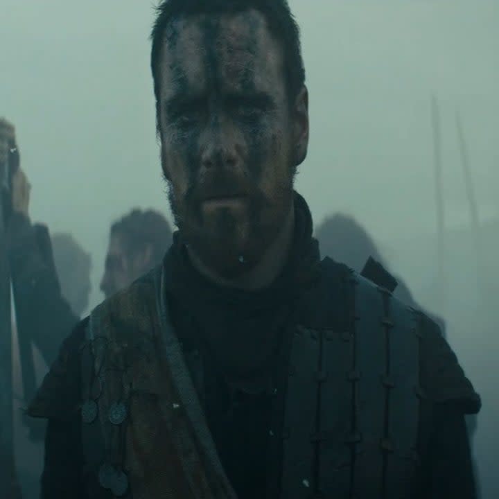 Michael Fassbender as Macbeth on a battlefield wearing leather armor