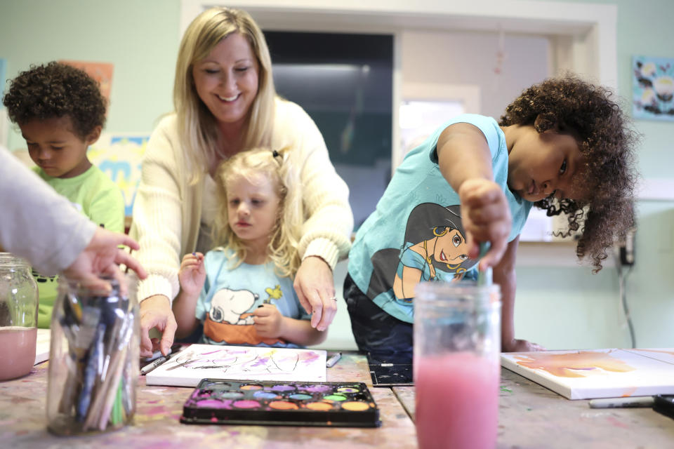 Winnie VanDusen, 3, paints at the Bumble Art Studio day care center, while the center director Amy Atkinson helps another child in Astoria, Ore., Friday, Sept. 2, 2022. From Oregon to New York, demand for child care far exceeds supply. Families are growing increasingly desperate as providers deal with staffing shortages exacerbated by the coronavirus pandemic as well as historically low pay worsened by inflation. (AP Photo/Craig Mitchelldyer)