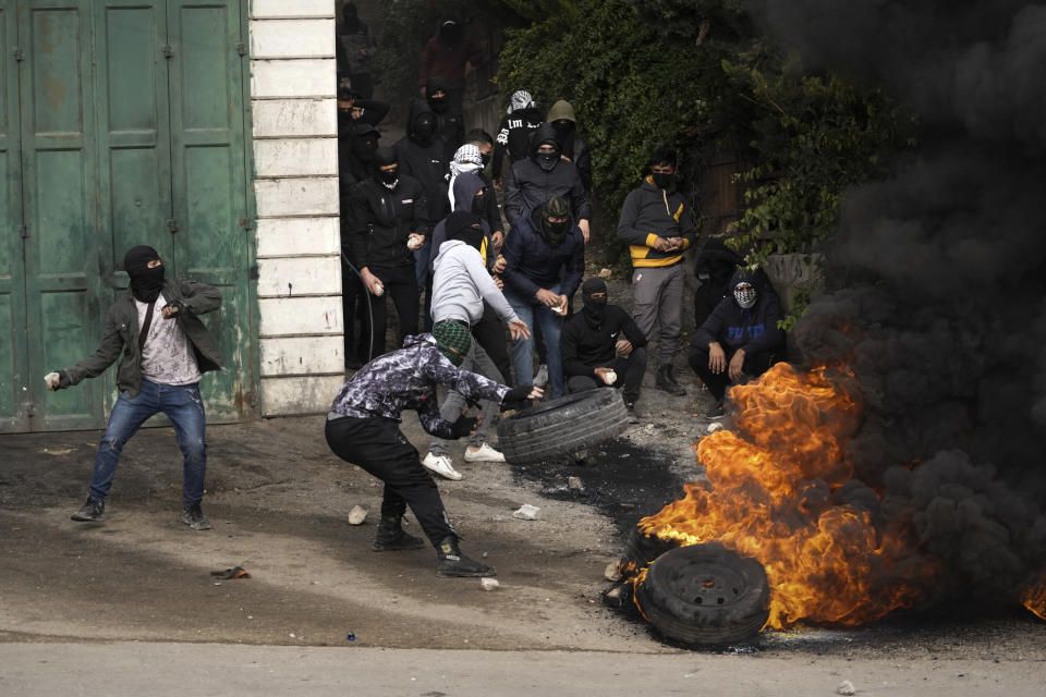 Masked Palestinians burn tires during clashes with Israeli security forces following the funeral of Mufid Khalil in the West Bank village of Beit Ummar, near Hebron, Tuesday, Nov. 29, 2022. Khalil was killed by Israeli fire in the occupied West Bank, the Palestinian Health Ministry said Tuesday. (AP Photo/Mahmoud Illean)