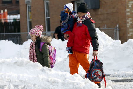 A man carries a child as they cross a snow covered street in the Queens borough of New York January 25, 2016. REUTERS/Shannon Stapleton