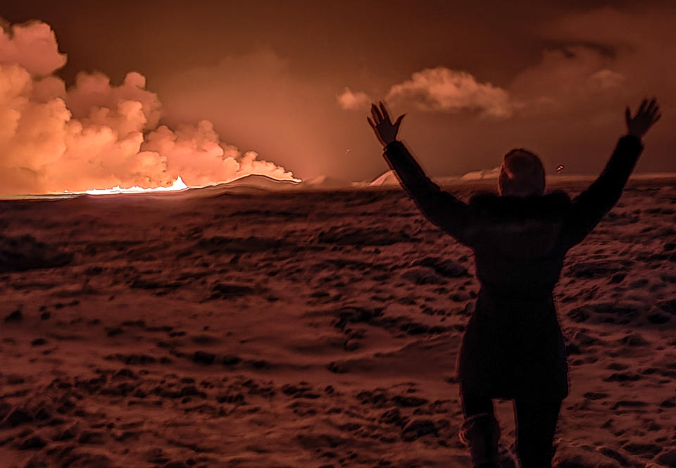 A local resident looks at smoke on December 18, 2023 as lava colors the night sky orange from a volcanic eruption on the Reykjanes peninsula 3 km north of Grindavik, in western Iceland on December 18, 2023. A volcanic eruption started on Monday night in Iceland , south of the capital.  Reykjavík, after an earthquake swarm, the Icelandic Meteorological Office reported.  (Photo by Kristin Elisabet Gunnarsdottir / AFP) (Photo by KRISTIN ELISABET GUNNARSDOTTIR/AFP via Getty Images)