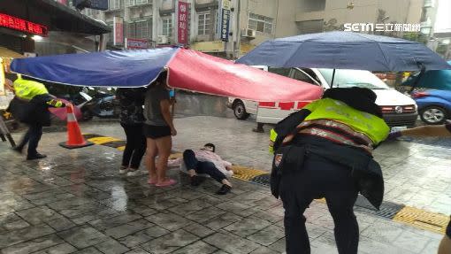 一名婦人因摔車倒在路上，一旁有2名少女拿著「500萬大傘」幫忙擋雨。