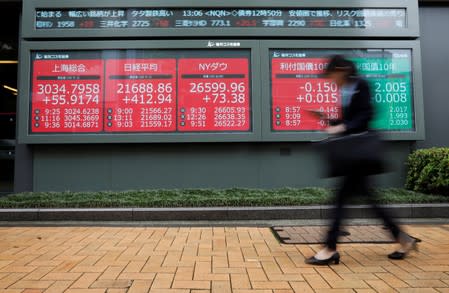 A woman walks past an electric screen showing world markets indices outside a brokerage in Tokyo